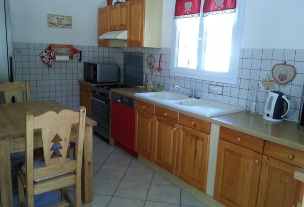 Une cuisine avec des meubles de rangement en bois, un évier, une cuisinière et une table à manger avec des chaises.