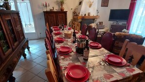 A dining area with a long table set for a meal, a fireplace, a television, and a sofa in the background.