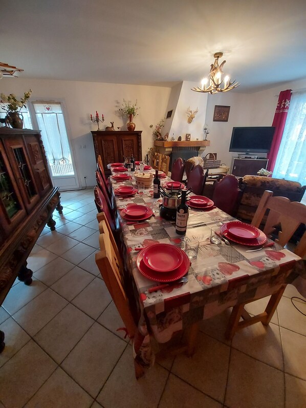 A dining area with a long table set for a meal, a fireplace, a television, and a sofa in the background. - CHALET 126 M² in PRALOUP (Uvernet-Fours)