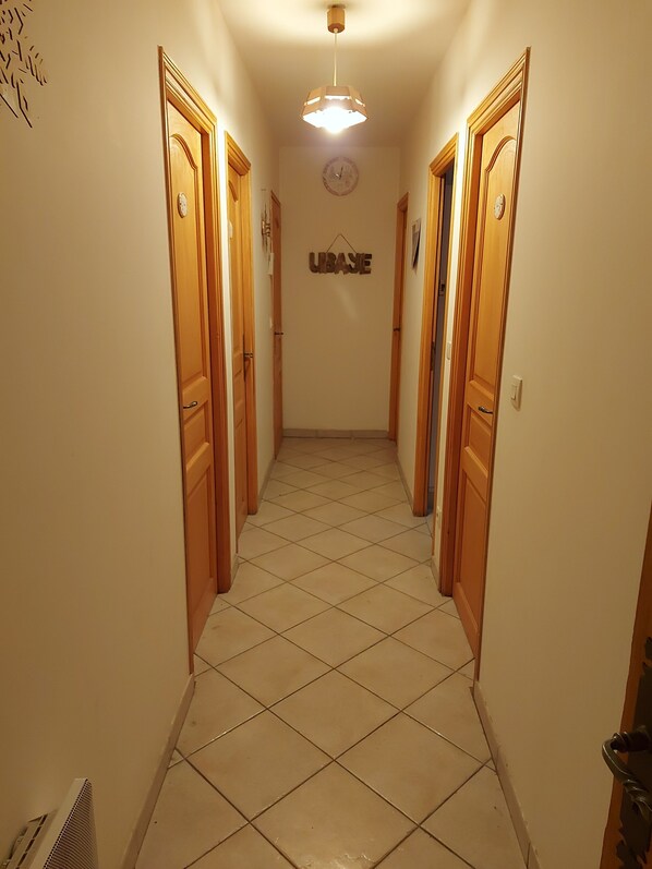 Un couloir avec des portes en bois, un sol carrelé et un luminaire au plafond.