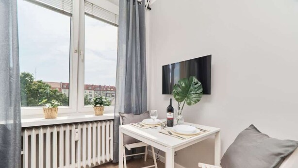 Ein kleiner Essbereich mit Tisch für zwei Personen, einem Topfpflanzen und einem an der Wand montierten Fernseher.
