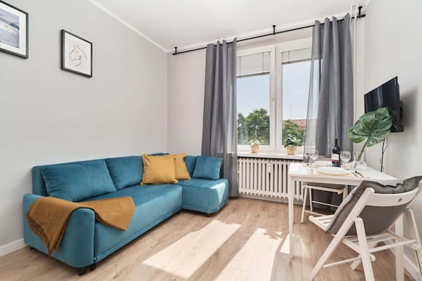 A modern living room with a blue sofa, a dining table, and a TV.