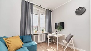 Ein modernes Wohnzimmer mit einem blauen Sofa, einem Esstisch, einem Fernseher und Blick auf die Stadt.