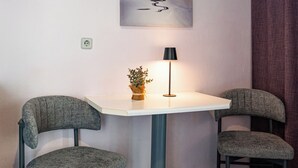 A small room with two chairs, a table, a lamp, a painting of a sailboat, and a power outlet. - Sand Garden Apart, Wi‑Fi & garden near the beach (Agios Dimitrios)