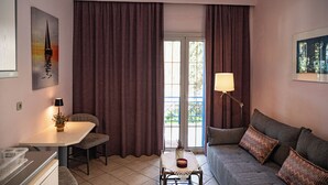 A living room with a sofa, a table, a lamp, and a view through a window. - Sand Garden Apart, Wi‑Fi & garden near the beach (Agios Dimitrios)