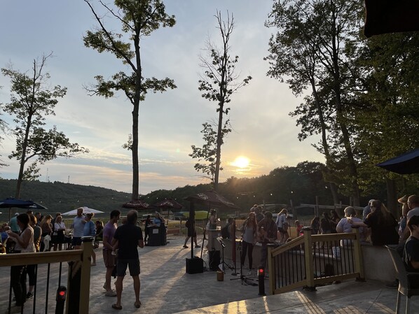 An outdoor event with people gathered around tables and chairs, with a sunset in the background.