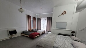 Ein Schlafzimmer mit zwei Einzelbetten, einem großen Bett, einem Heizkörper, einem Fernseher und einem Fenster mit Vorhängen.
