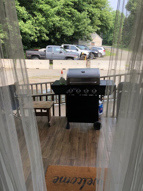 A balcony with a grill, a wooden table, and a chair.