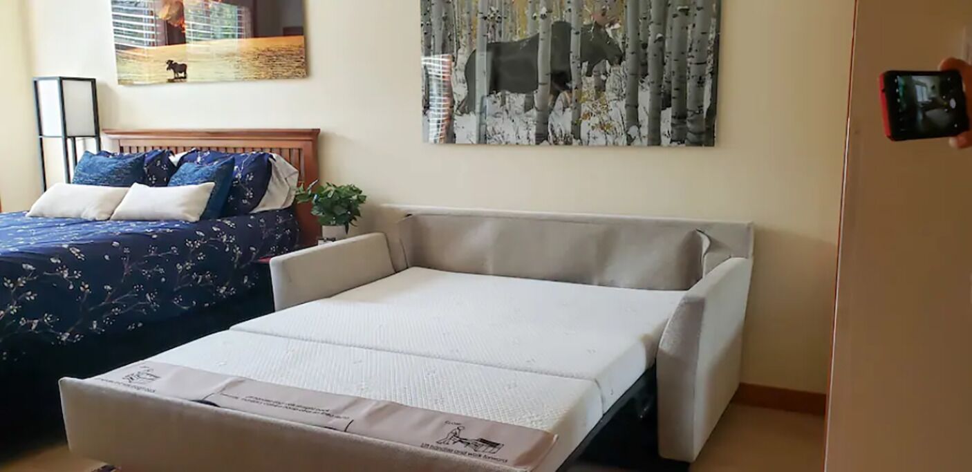 A hotel room with a bed, a sofa, a small table, and a painting on the wall.