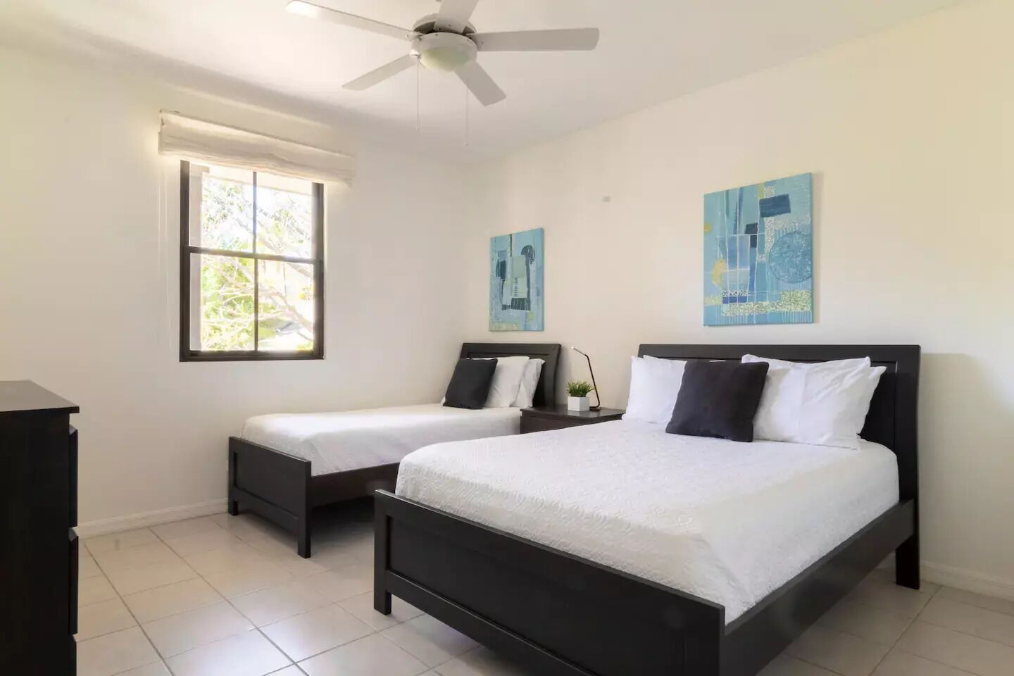 A bedroom with two beds, a ceiling fan, and artwork on the walls.