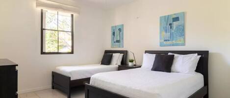 A bedroom with two beds, a ceiling fan, and artwork on the walls.