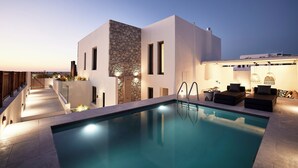 Un espace piscine moderne agrémenté d’un mur d’accent en pierre, de coins salon extérieurs et d’un escalier menant à un niveau supérieur.