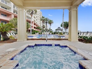 Un espace avec un jacuzzi, une piscine, des palmiers et un bâtiment doté de balcons en arrière-plan.