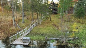 Una cabaña en un bosque con un muelle de madera que conduce a un muelle pequeño.