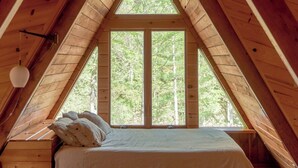 Un dormitorio tipo loft con techo inclinado, una cama, un ventilador de techo y un ventanal grande.
