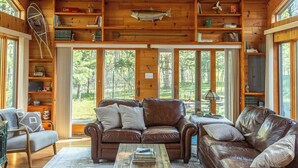 Interior acogedor de una cabaña con paredes de madera, ventilador de techo, una gran decoración de pez, sofás de cuero y una estantería.
