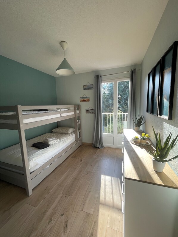 A room with a bunk bed, a small table with potted plants, a window with curtains, and a ceiling light. - Peaceful Stay in Ste Maxime – 2BR Apartment with Pool, A/C, Balcony, Parking (Sainte-Maxime)