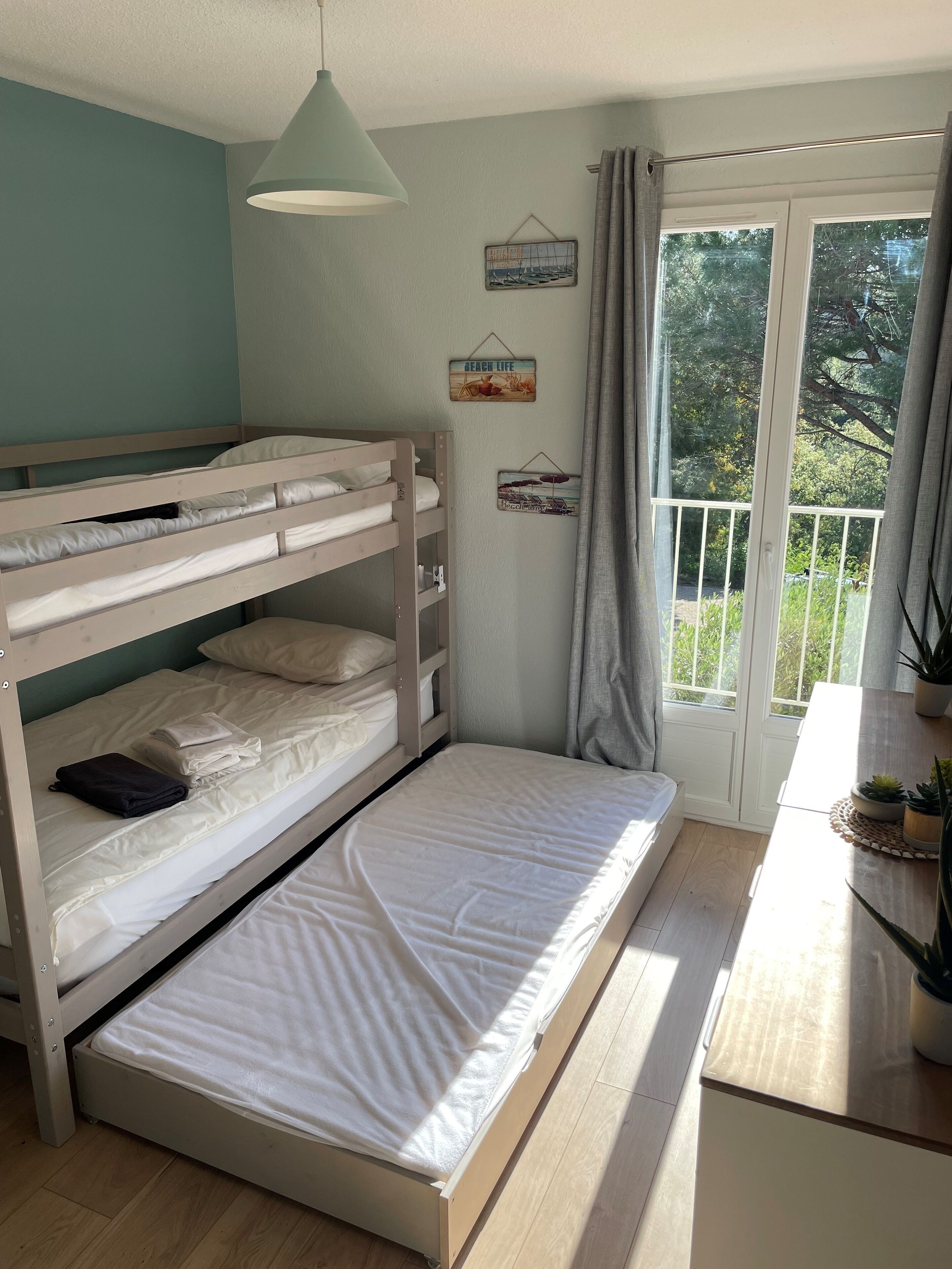 Una stanza con un letto a castello, una lampada a sospensione, una finestra con tende e vista sul verde.
