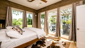Une chambre dotée d’un grand lit, d’un ventilateur de plafond et offrant une vue sur l’extérieur grâce à de grandes portes vitrées.