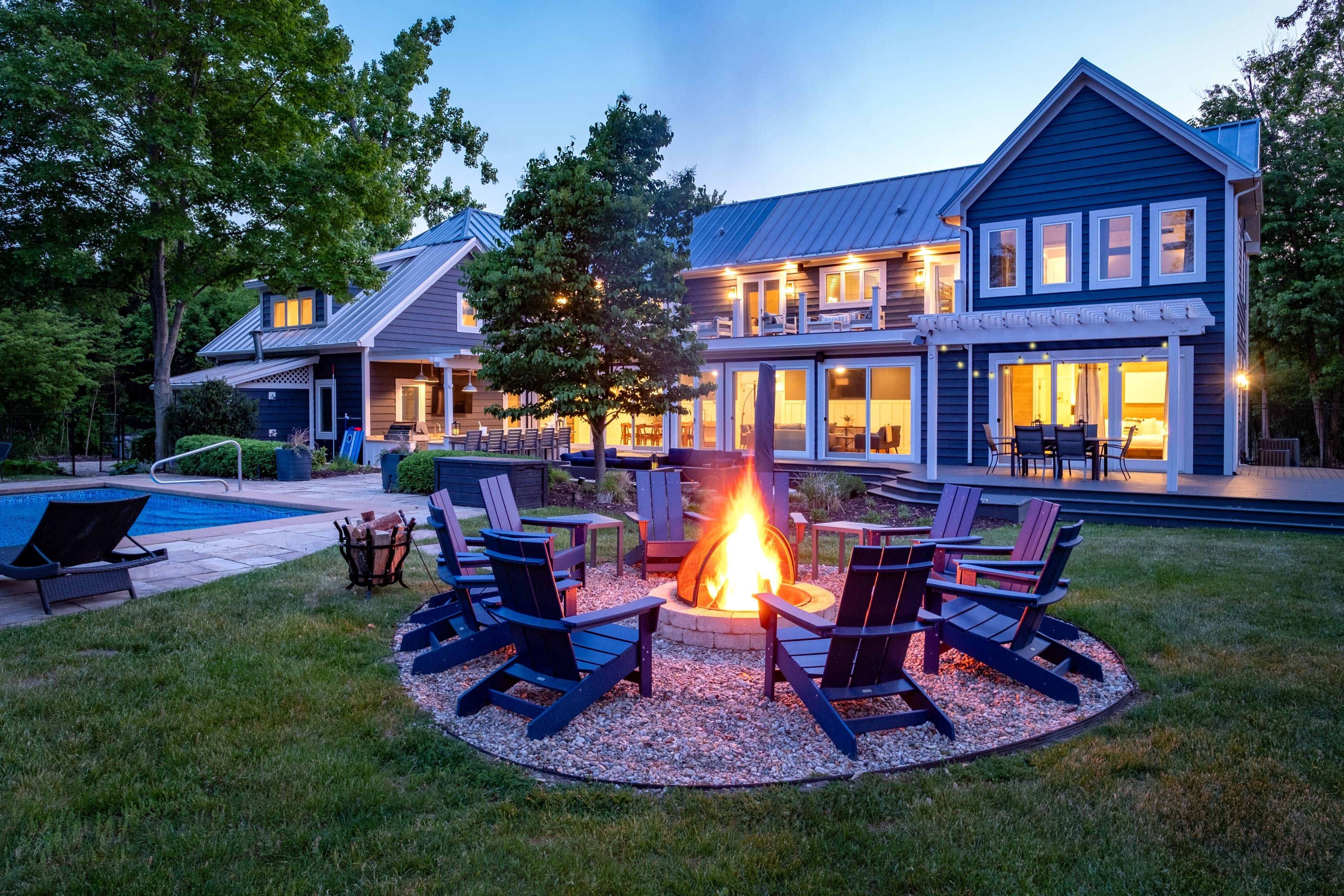A large house with a fire pit in the backyard, surrounded by outdoor seating.