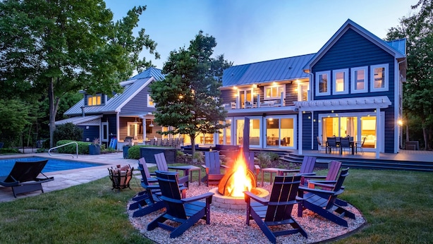 Une grande maison avec un foyer extérieur dans le jardin, entourée d’espaces de détente en plein air.