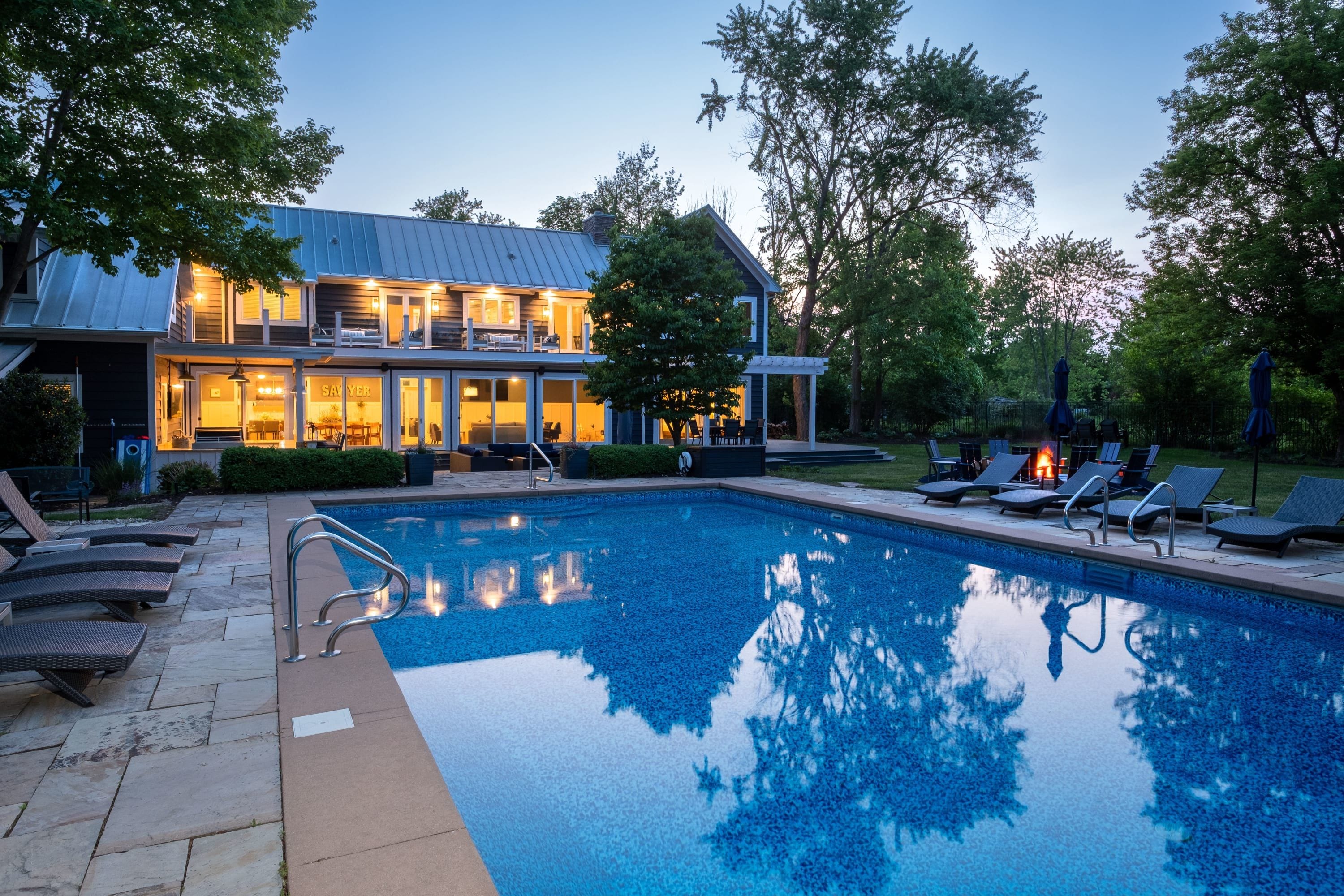 A two-story house with a swimming pool, outdoor seating, and a fire pit.