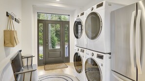 Une buanderie avec une porte d’entrée, un banc, un porte-manteau et des machines à laver superposées.