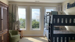Un dormitorio con literas, un sillón verde, una lámpara y vistas a árboles a través de amplios ventanales.