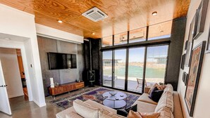Una sala moderna con un sofá grande, una mesa de centro y un televisor montado en la pared. Un ventanal grande ofrece vistas al exterior.