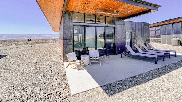 Un edificio moderno con fachada de concreto, grandes puertas de vidrio y un patio cubierto con sillones de descanso.