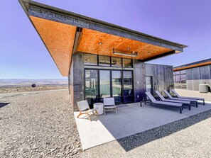 Un edificio moderno con fachada de concreto, grandes puertas de vidrio y un patio cubierto con sillones de descanso.