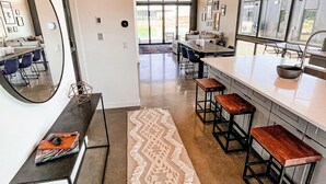 Una cocina moderna con una encimera amplia, taburetes de bar y un gran ventanal que proporciona luz natural.