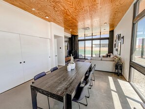 Un espace repas moderne avec une table et des chaises en bois, un canapé et une grande fenêtre donnant sur l’extérieur.