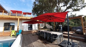 A wooden deck with a pool, outdoor seating, and red umbrellas.