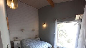 A bedroom with a bed, bedside tables, a wall-mounted light, and a window with curtains. - Villa Le Repère, quiet area, air-conditioned with swimming pool (SAINT AYGULF)