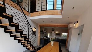 A spacious dining area with a long wooden table and black chairs, a staircase with wooden steps and black railings, and a kitchen area in the background. - Villa Le Repère, quiet area, air-conditioned with swimming pool (SAINT AYGULF)