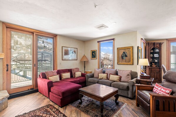 A spacious living room with a red sectional sofa, a gray sofa, and a brown leather chair. There is a wooden coffee table and a rug on the floor.