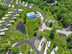 Vista aérea de un camping con vehículos recreativos, una piscina y un lago.