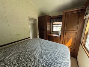 A bedroom with a patterned bedspread, a wooden dresser, a mirror, and a window with blinds.