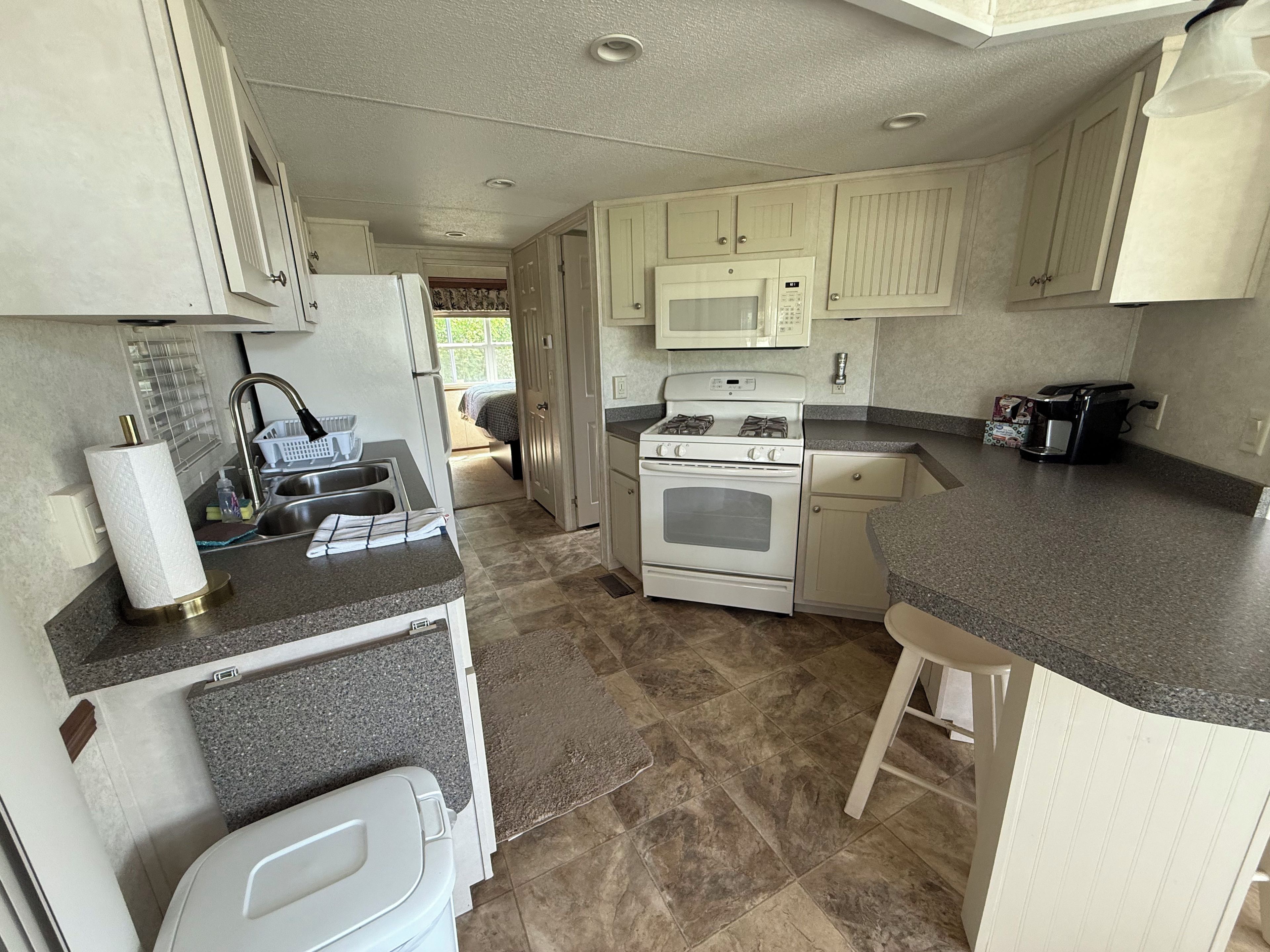 A compact kitchen with a sink, stove, microwave, and a coffee maker.