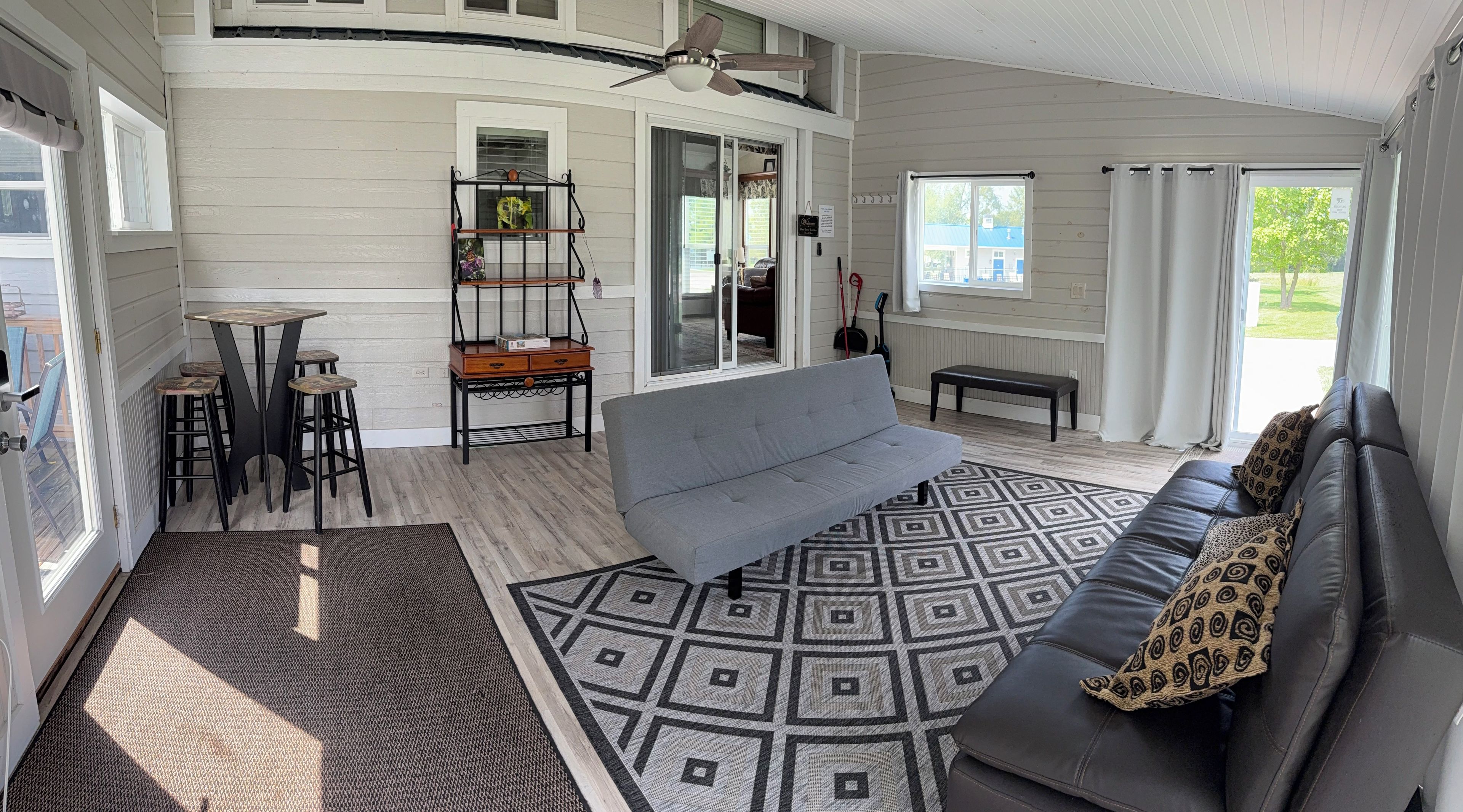 A spacious living area with a grey sofa, a patterned rug, and a dining table with stools.