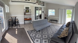 A spacious living area with a grey sofa, a patterned rug, and a dining table with stools.