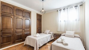 Une chambre d’hôtel avec deux lits, des armoires en bois, une table de chevet et une fenêtre avec des rideaux.