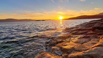 Kallioinen rantaviiva, jonka yllä auringonlasku heijastuu vesistöstä.