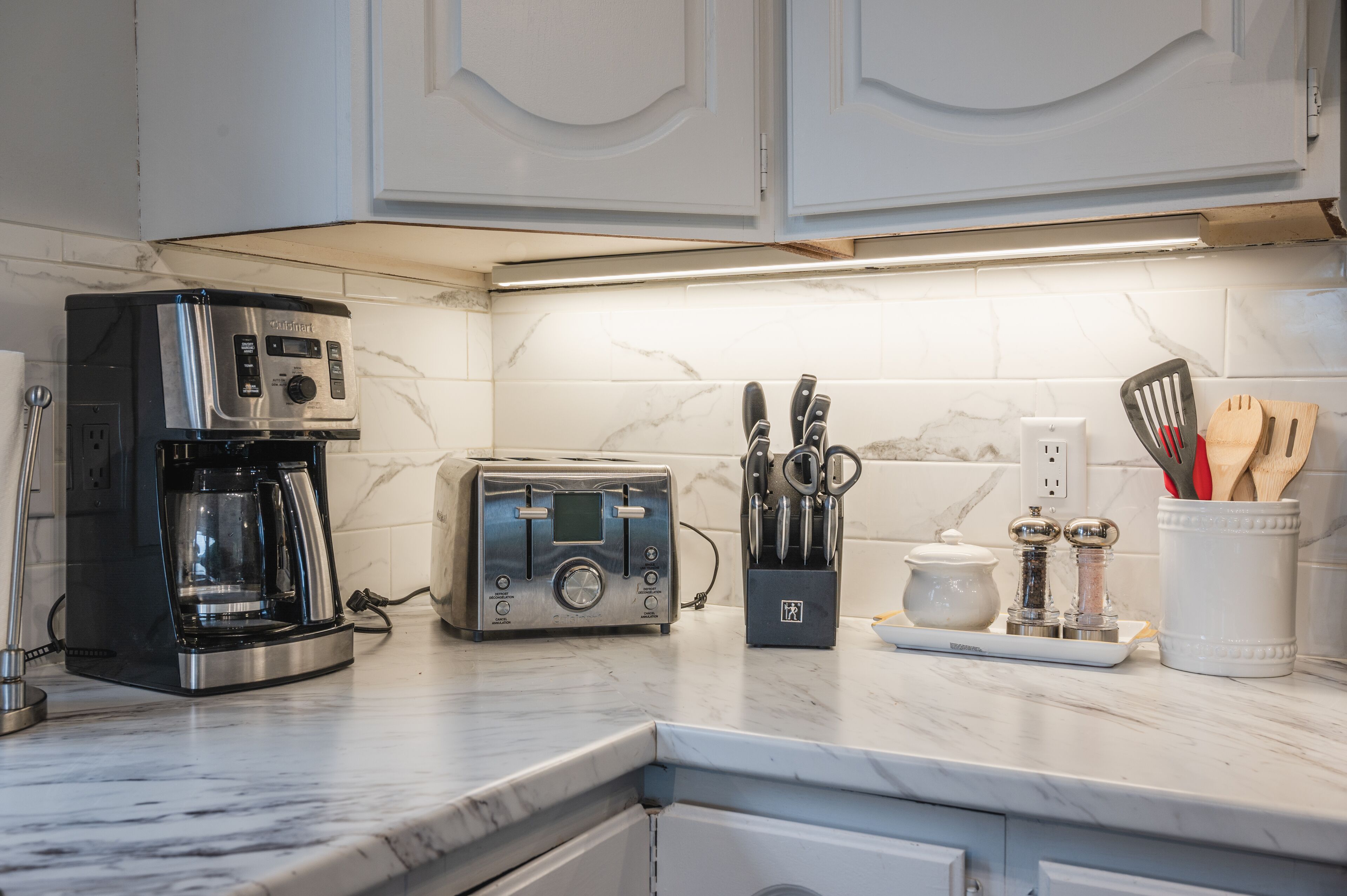 A kitchen with a coffee maker, toaster, knife block, salt and pepper shakers, and a white cabinet.