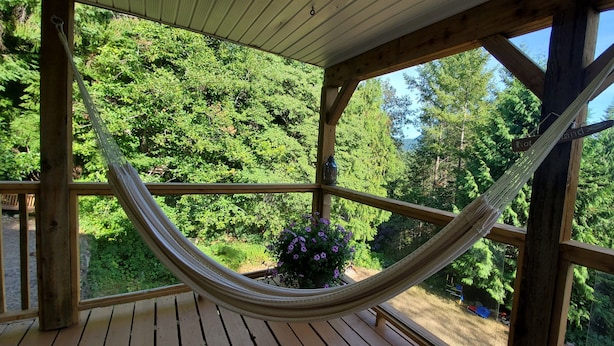 Een houten terras met een hangmat en uitzicht op een bebost gebied.