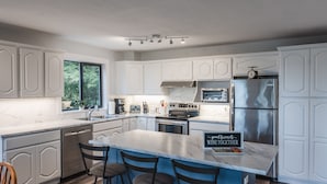Een moderne keuken met witte kasten, een marmeren aanrecht en een centraal eiland met barstoelen.