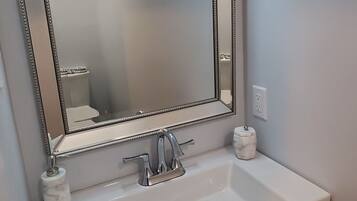 A bathroom with a white sink, dark cabinets, a large mirror, and a wall-mounted light fixture.