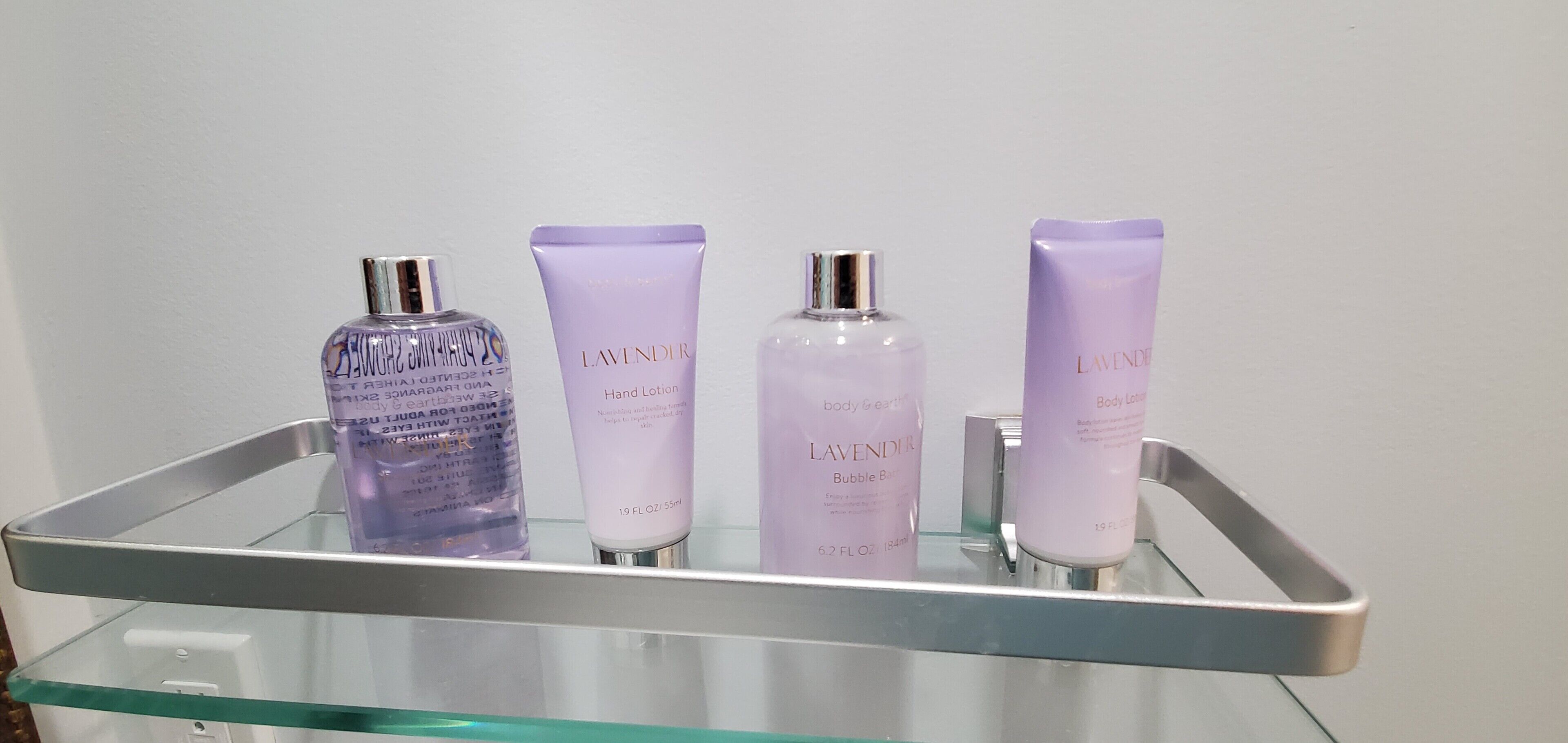En hylla i badrummet med tre flaskor lavendeldoftande kroppslotion och en genomskinlig glasflaska.