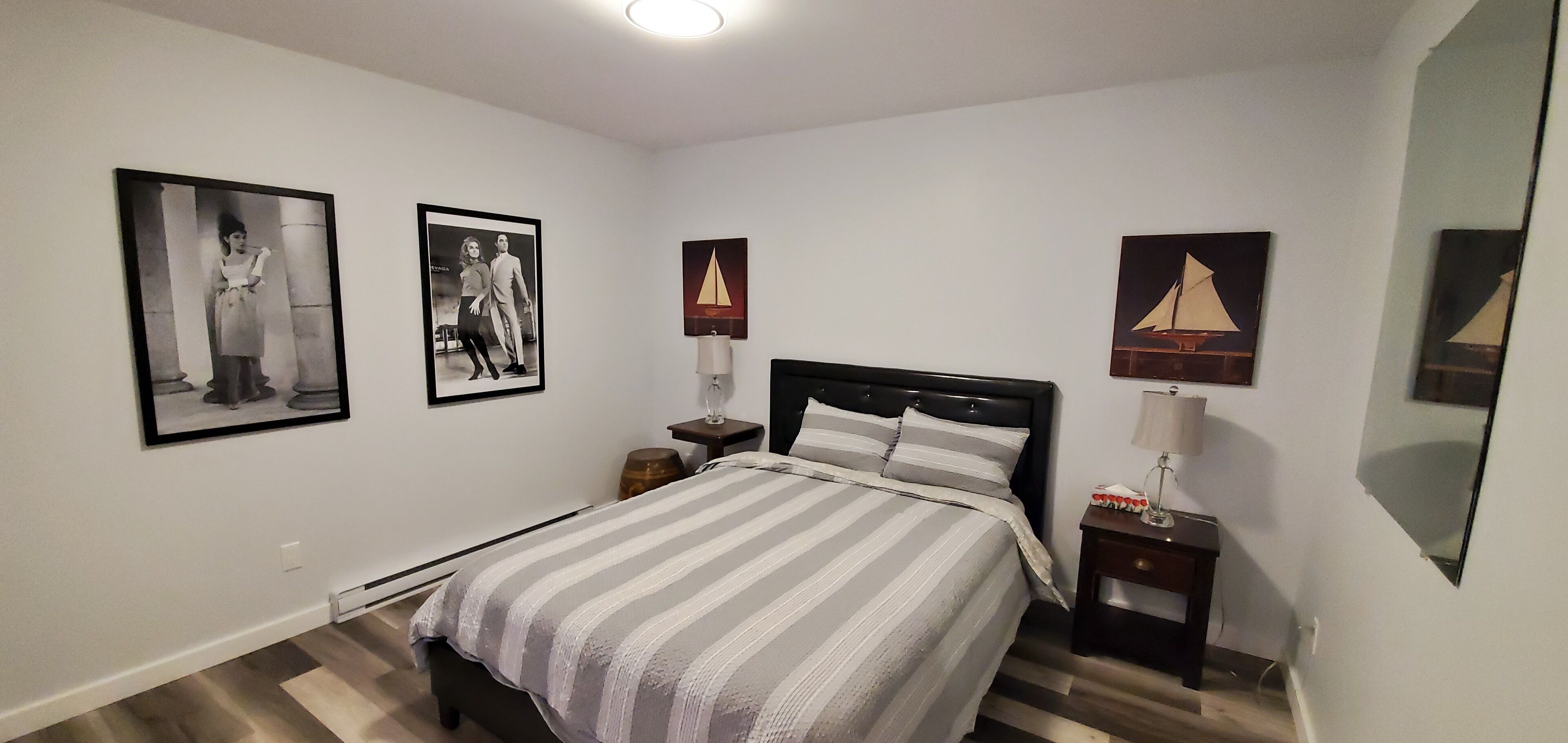 Ein Schlafzimmer mit einem Bett, zwei Nachttischen, einem Spiegel und drei gerahmten Bildern an der Wand.